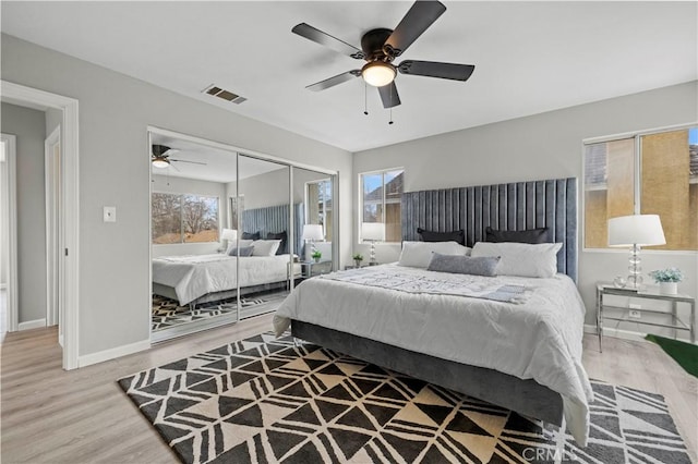 bedroom with multiple windows, ceiling fan, wood-type flooring, and a closet