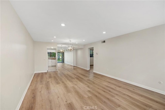 spare room featuring light wood-type flooring and an inviting chandelier