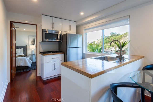 kitchen featuring appliances with stainless steel finishes, white cabinetry, sink, dark hardwood / wood-style flooring, and kitchen peninsula