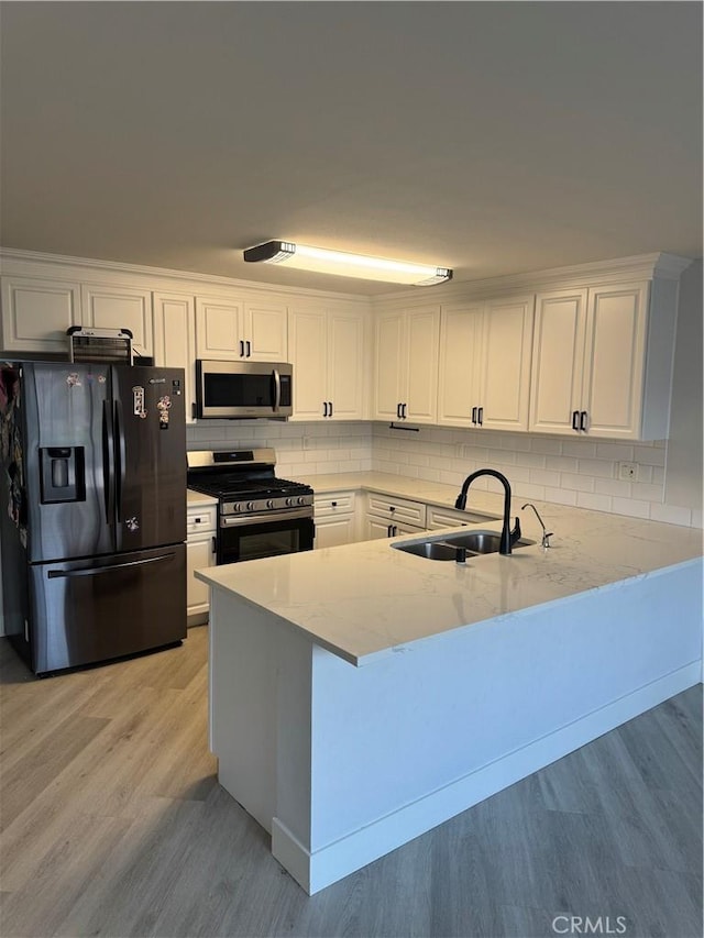 kitchen with sink, white cabinetry, light hardwood / wood-style flooring, kitchen peninsula, and stainless steel appliances