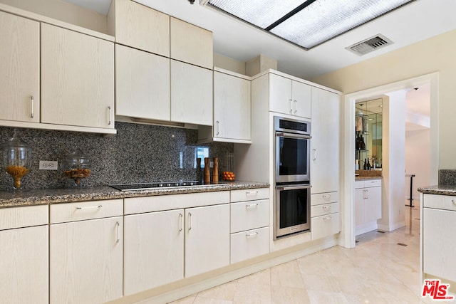 kitchen with black electric stovetop, dark stone counters, double oven, and decorative backsplash