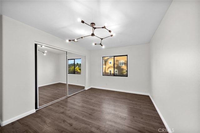 unfurnished bedroom featuring dark hardwood / wood-style flooring, a closet, and a notable chandelier