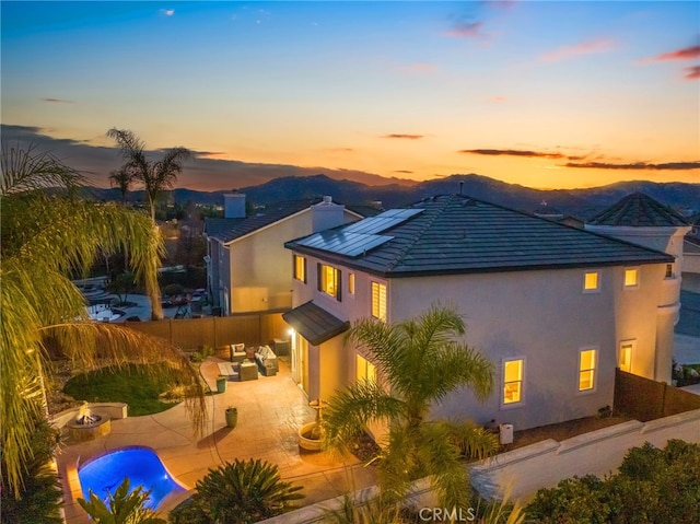 back house at dusk featuring solar panels, a mountain view, an outdoor living space with a fire pit, and a patio area