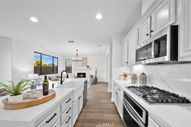 kitchen featuring sink, hanging light fixtures, stainless steel appliances, decorative backsplash, and white cabinets