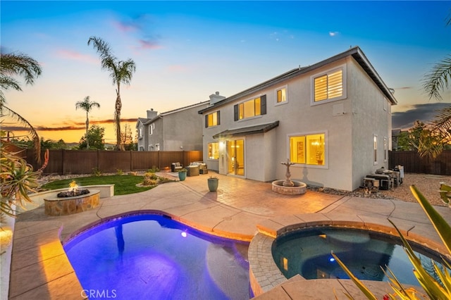 pool at dusk featuring an in ground hot tub, a patio, and a fire pit