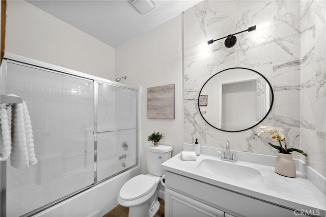 full bathroom with vanity, tile walls, enclosed tub / shower combo, and toilet