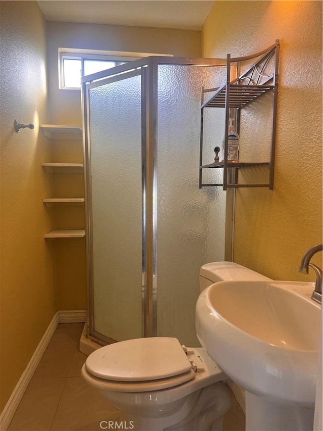 full bathroom featuring toilet, a stall shower, a sink, baseboards, and tile patterned floors