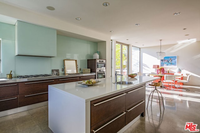 kitchen with pendant lighting, appliances with stainless steel finishes, sink, a center island with sink, and dark brown cabinets