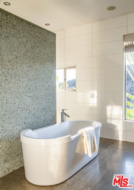 bathroom featuring a healthy amount of sunlight, a bath, and tile walls