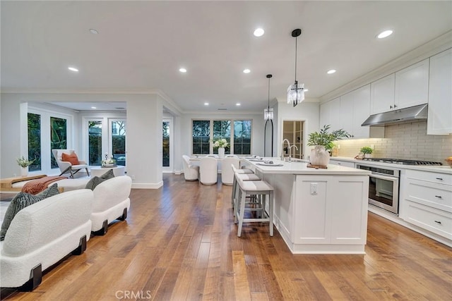 kitchen featuring appliances with stainless steel finishes, pendant lighting, a kitchen island with sink, decorative backsplash, and white cabinets