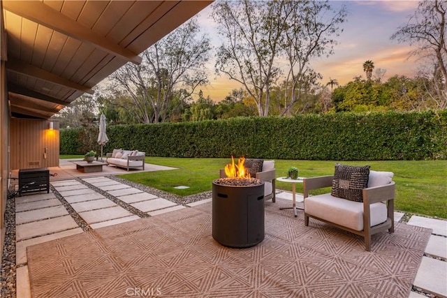 patio terrace at dusk featuring a lawn and an outdoor living space with a fire pit