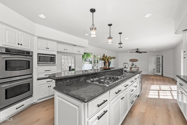 kitchen featuring white cabinets, appliances with stainless steel finishes, a center island, light hardwood / wood-style floors, and hanging light fixtures