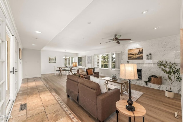 living room with ceiling fan with notable chandelier, a tile fireplace, and light hardwood / wood-style flooring