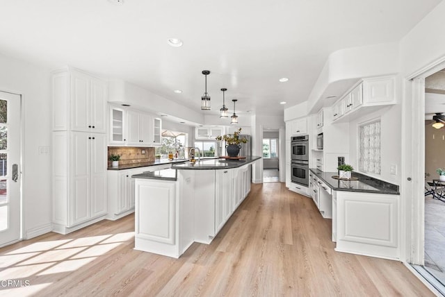 kitchen featuring stainless steel appliances, white cabinets, dark countertops, light wood-type flooring, and backsplash