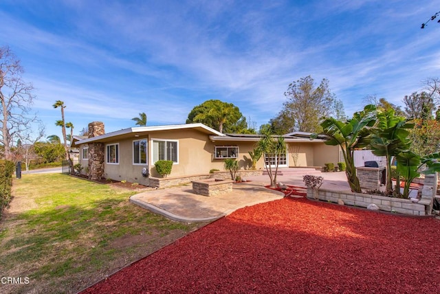 rear view of house with stucco siding, a yard, solar panels, a chimney, and a patio area