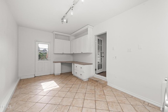 kitchen with baseboards, light tile patterned floors, built in desk, rail lighting, and white cabinets