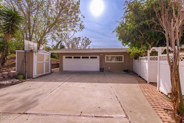 garage with driveway, a shed, and fence