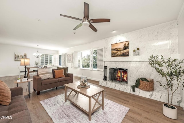 living area with ceiling fan with notable chandelier, wood finished floors, baseboards, and a high end fireplace