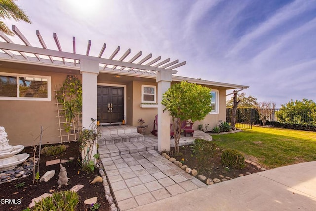 entrance to property featuring a yard, fence, a pergola, and stucco siding