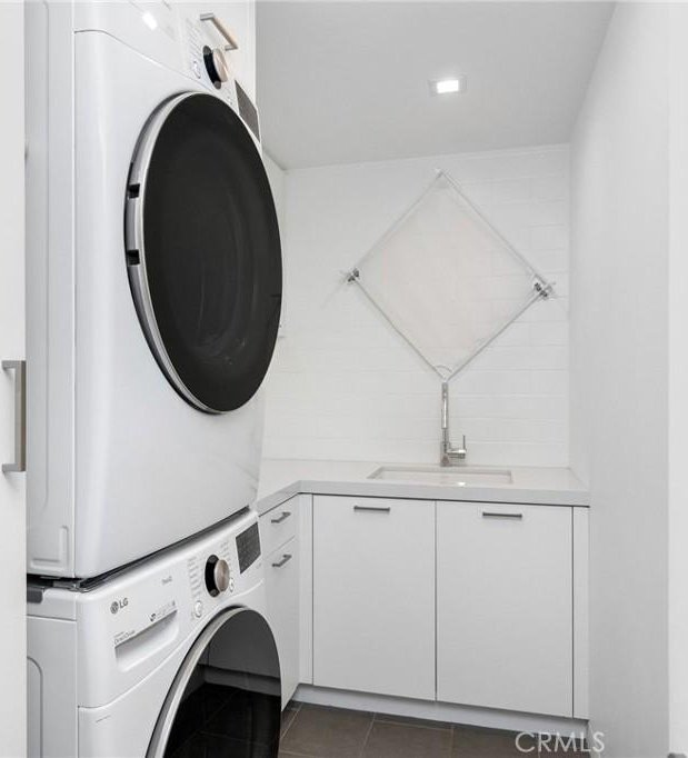 laundry room with cabinets, stacked washing maching and dryer, dark tile patterned flooring, and sink