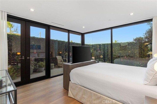 bedroom featuring multiple windows, a wall of windows, light hardwood / wood-style floors, and french doors