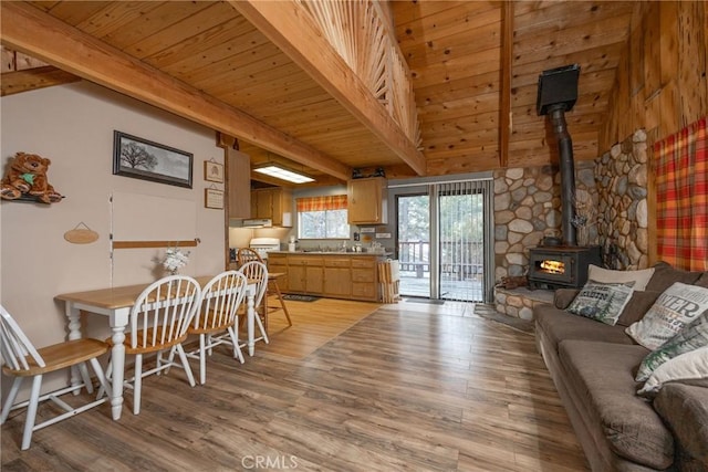 interior space with a wood stove, wooden ceiling, beam ceiling, and light hardwood / wood-style floors