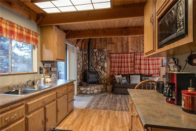 kitchen featuring beamed ceiling, sink, a wood stove, wood ceiling, and light wood-type flooring