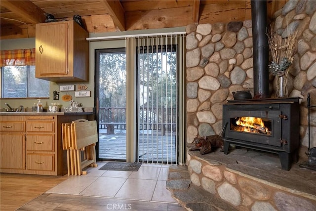 doorway to outside with beam ceiling, light tile patterned floors, wood ceiling, and a wood stove