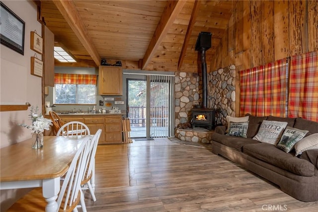 living room with beam ceiling, wooden ceiling, light hardwood / wood-style floors, and a wood stove