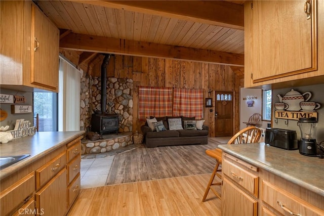 kitchen featuring plenty of natural light, beam ceiling, light hardwood / wood-style floors, and a wood stove