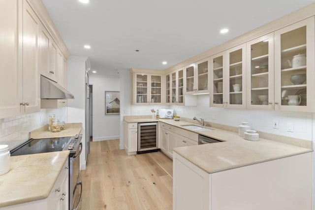 kitchen with appliances with stainless steel finishes, sink, wine cooler, light stone counters, and light wood-type flooring