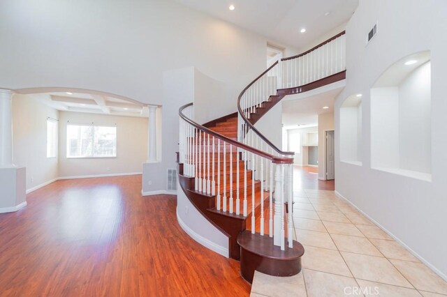 stairs with coffered ceiling, beam ceiling, a high ceiling, and ornate columns