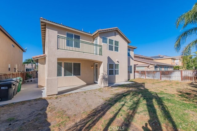 rear view of property featuring a balcony, a yard, and a patio area