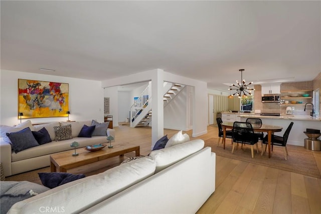 living room with a notable chandelier, light wood-type flooring, and sink