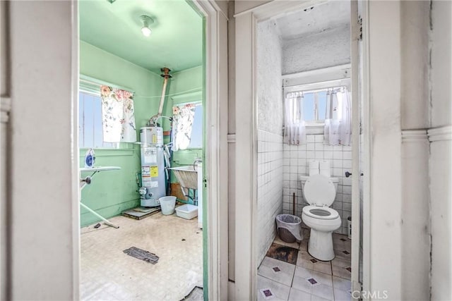 bathroom featuring water heater, tile patterned flooring, sink, tile walls, and toilet