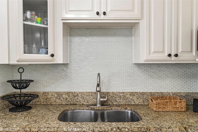 kitchen with light stone counters, white cabinets, sink, and backsplash