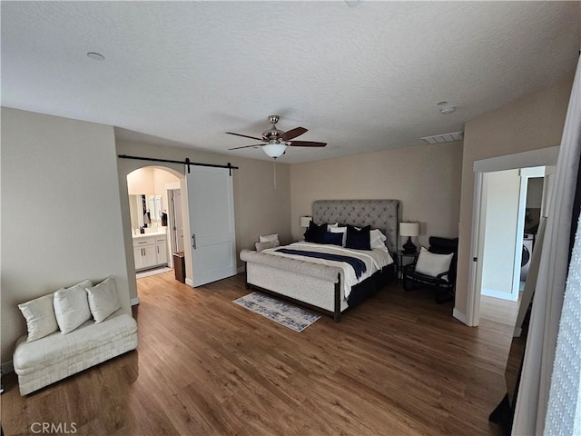 bedroom with washer / dryer, ensuite bath, dark hardwood / wood-style floors, ceiling fan, and a barn door