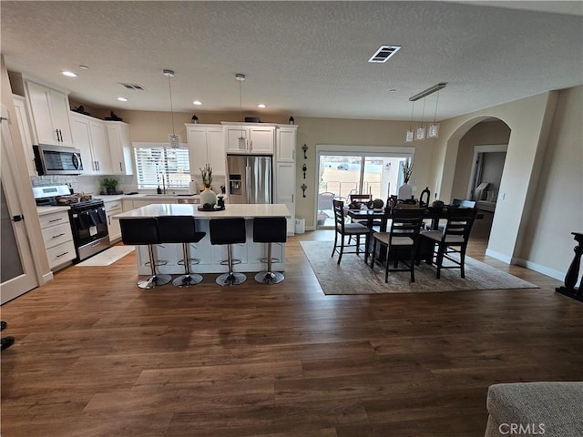 kitchen with white cabinetry, decorative light fixtures, a center island, a textured ceiling, and stainless steel appliances