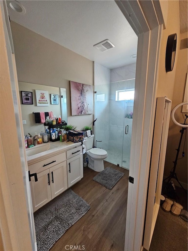 bathroom featuring wood-type flooring, toilet, a shower with door, and vanity