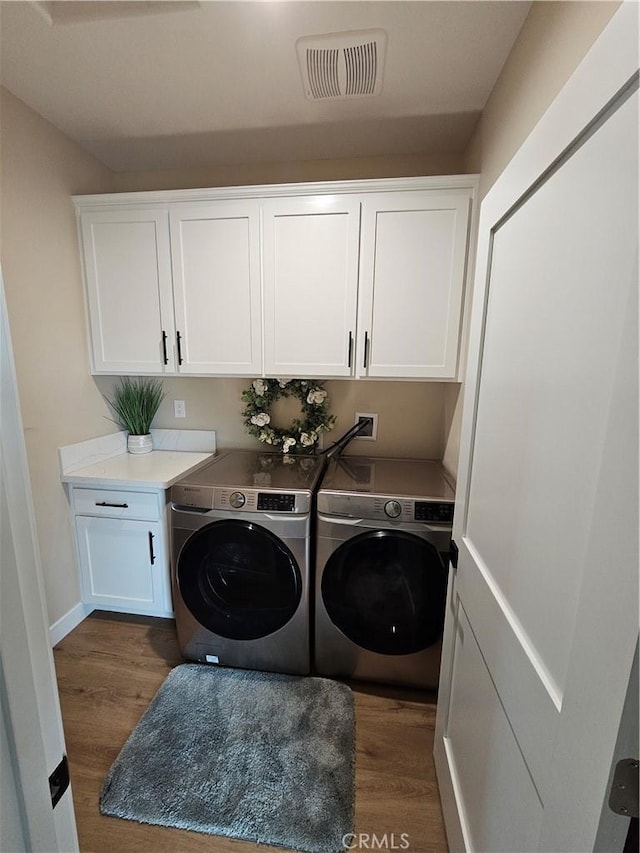 washroom with dark hardwood / wood-style floors, cabinets, and washing machine and clothes dryer