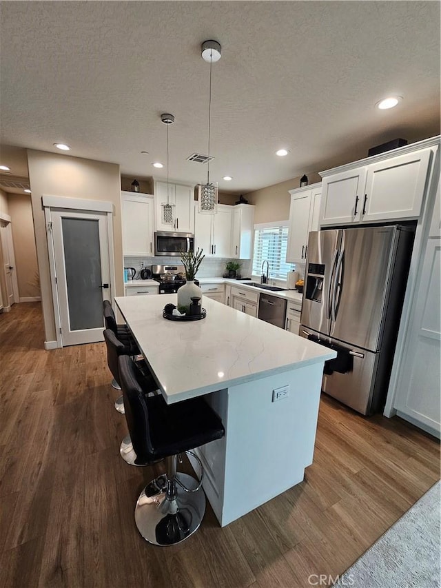 kitchen featuring appliances with stainless steel finishes, wood-type flooring, white cabinets, hanging light fixtures, and a center island