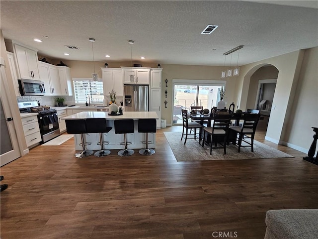 kitchen with a kitchen island, white cabinets, hanging light fixtures, stainless steel appliances, and a textured ceiling