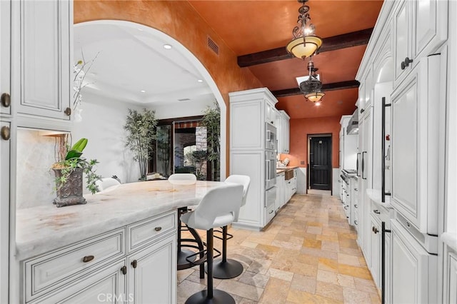 kitchen featuring beam ceiling, light stone counters, white cabinets, and a kitchen breakfast bar