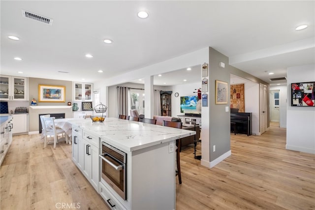 kitchen featuring a kitchen island, white cabinetry, a kitchen breakfast bar, stainless steel oven, and light stone counters