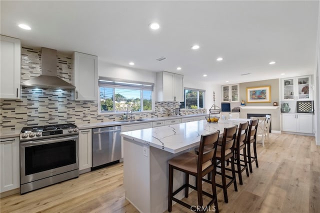 kitchen with wall chimney exhaust hood, sink, white cabinetry, a kitchen island, and stainless steel appliances