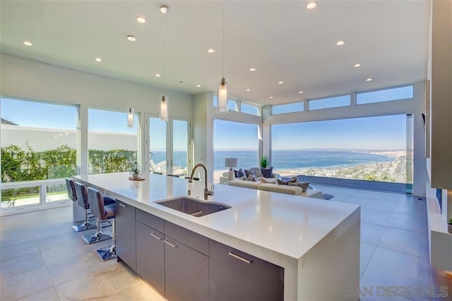 kitchen with sink, gray cabinets, a water view, decorative light fixtures, and a large island with sink