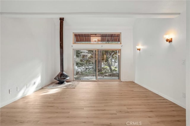 interior space featuring a wood stove, beamed ceiling, and light wood-type flooring