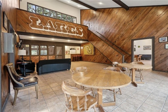 dining area featuring a towering ceiling, wooden walls, beamed ceiling, and light tile patterned floors