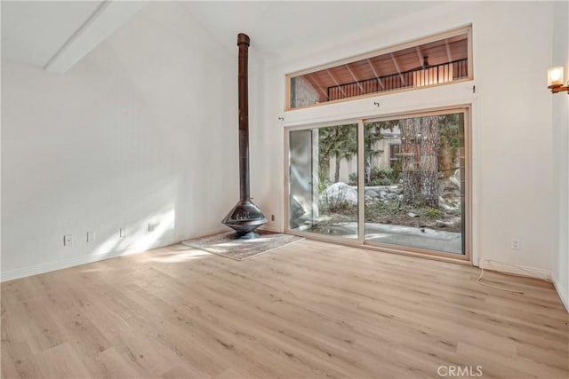 unfurnished living room featuring a wood stove, high vaulted ceiling, beam ceiling, and light hardwood / wood-style floors