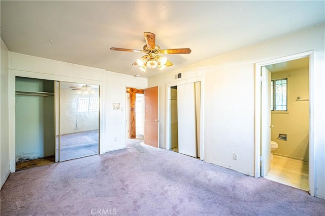 unfurnished bedroom with ceiling fan, ensuite bathroom, and light carpet